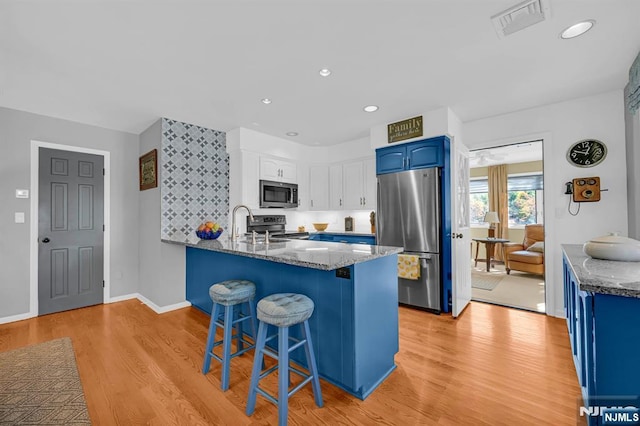 kitchen with dark stone countertops, stainless steel appliances, blue cabinetry, and a peninsula