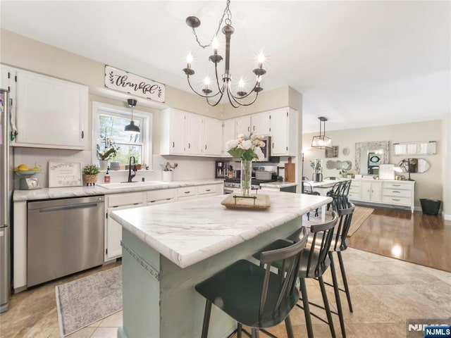 kitchen with a kitchen island, appliances with stainless steel finishes, light stone countertops, white cabinetry, and a sink