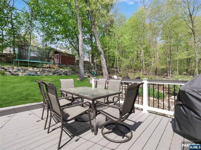 deck with a trampoline, a lawn, grilling area, a storage shed, and outdoor dining space