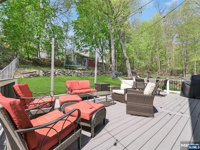 wooden deck featuring a yard, a trampoline, fence, and an outdoor living space