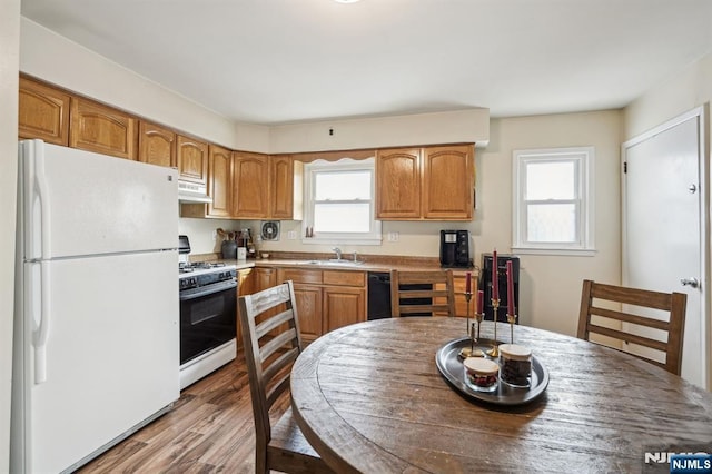 kitchen with white appliances, light wood-style flooring, light countertops, under cabinet range hood, and a sink