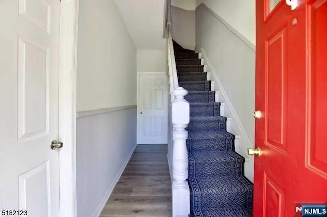 staircase with a wainscoted wall and wood finished floors