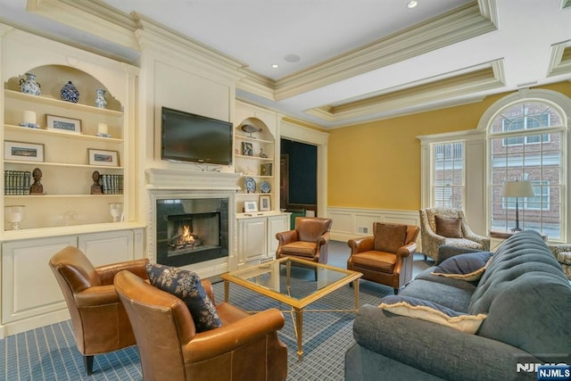 living area featuring wainscoting, a glass covered fireplace, ornamental molding, built in shelves, and a decorative wall