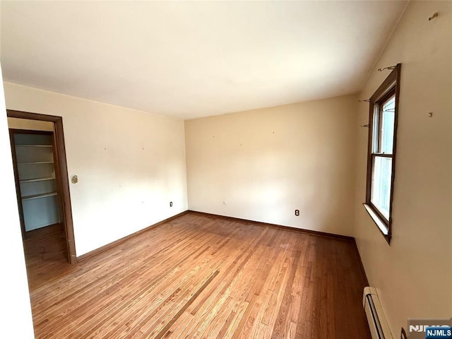 spare room with a baseboard radiator, light wood-style flooring, and baseboards