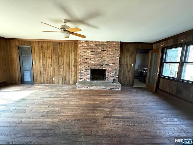 unfurnished living room with a brick fireplace, a ceiling fan, dark wood-type flooring, crown molding, and wood walls