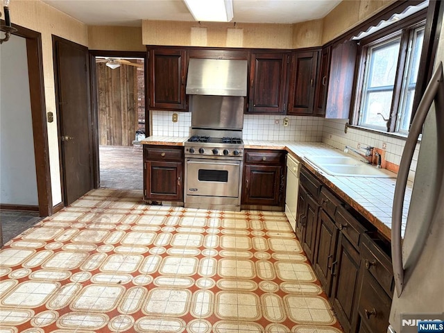 kitchen featuring dark brown cabinetry, premium range, a sink, ventilation hood, and tile counters