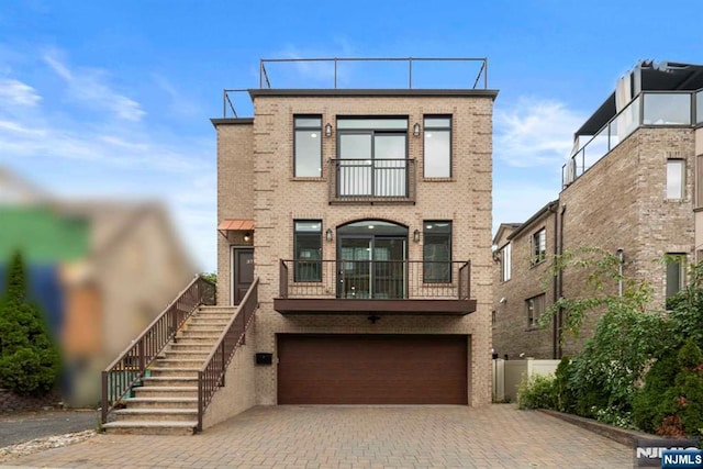 view of front facade featuring a balcony, a garage, brick siding, stairs, and decorative driveway