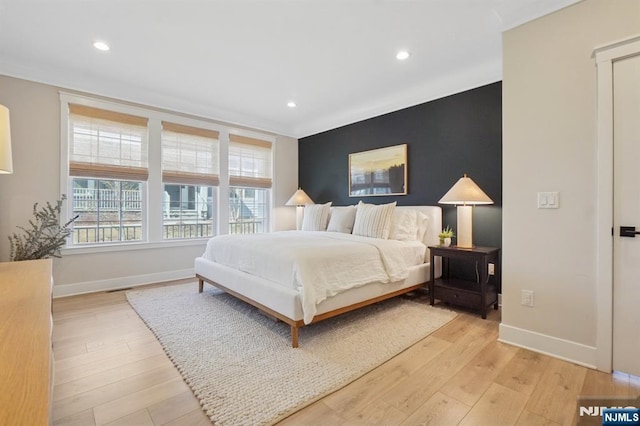 bedroom with baseboards, an accent wall, and light wood-style floors