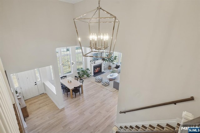 entryway with a towering ceiling, wood finished floors, a chandelier, a warm lit fireplace, and baseboards