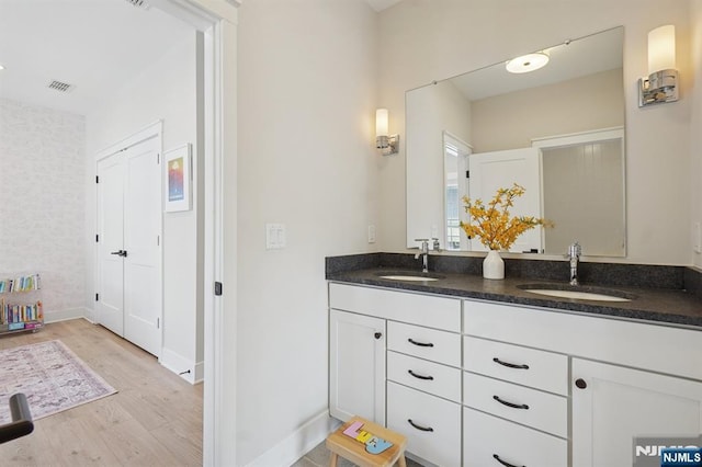 full bath with double vanity, a sink, baseboards, and wood finished floors