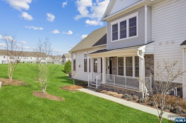 exterior space with covered porch, a shingled roof, stone siding, and a lawn