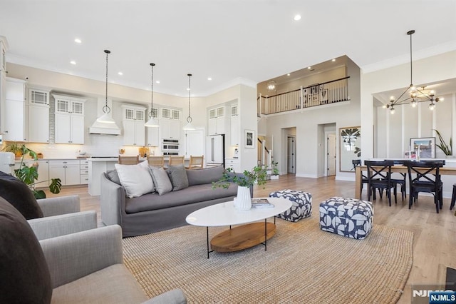 living room featuring a notable chandelier, crown molding, recessed lighting, light wood-style flooring, and a towering ceiling