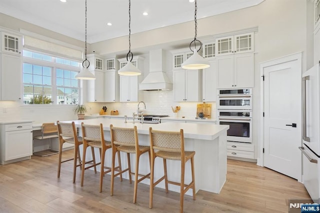 kitchen with tasteful backsplash, white appliances, a center island with sink, and custom range hood