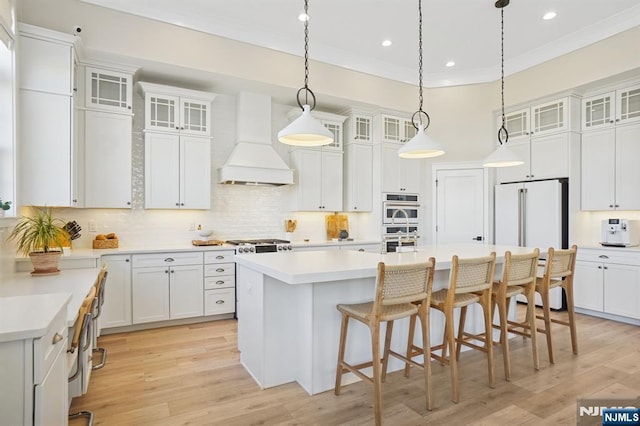 kitchen with high end white refrigerator, a breakfast bar, crown molding, a kitchen island with sink, and premium range hood