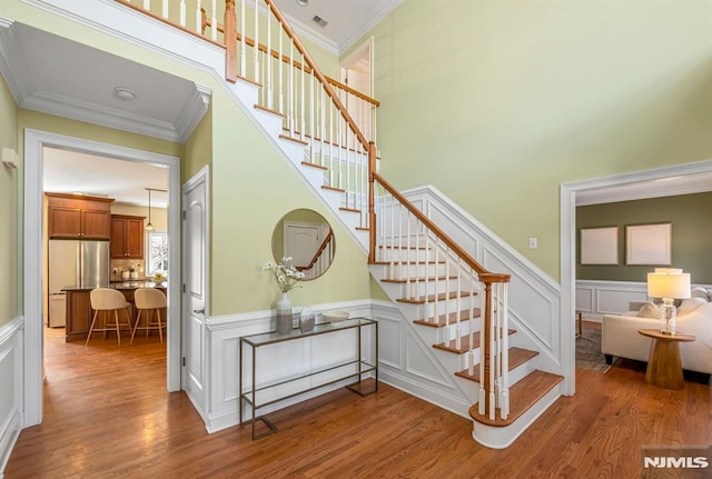 stairs featuring a wainscoted wall, ornamental molding, wood finished floors, and a towering ceiling