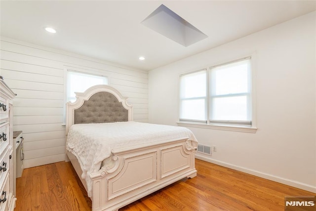 bedroom featuring baseboards, visible vents, light wood-type flooring, wood walls, and recessed lighting