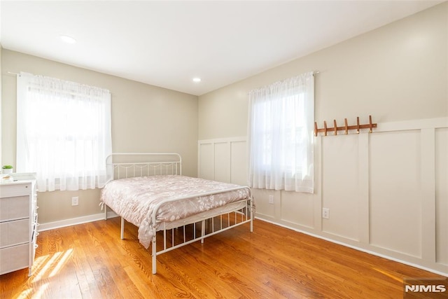 bedroom with recessed lighting, multiple windows, a decorative wall, and wood finished floors