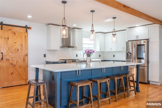 kitchen with light countertops, a barn door, white cabinetry, wall chimney range hood, and stainless steel fridge