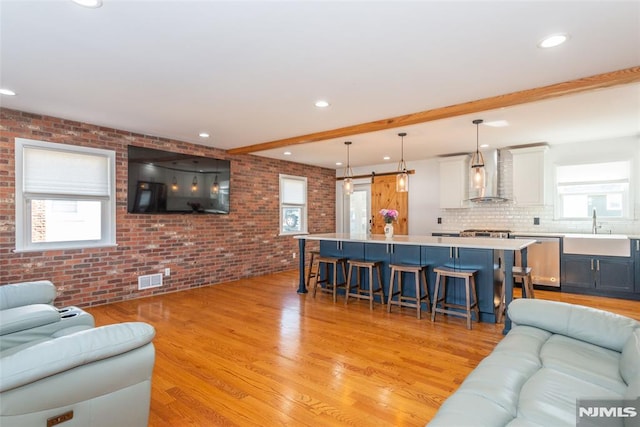 living area featuring brick wall, a barn door, light wood-type flooring, and a healthy amount of sunlight