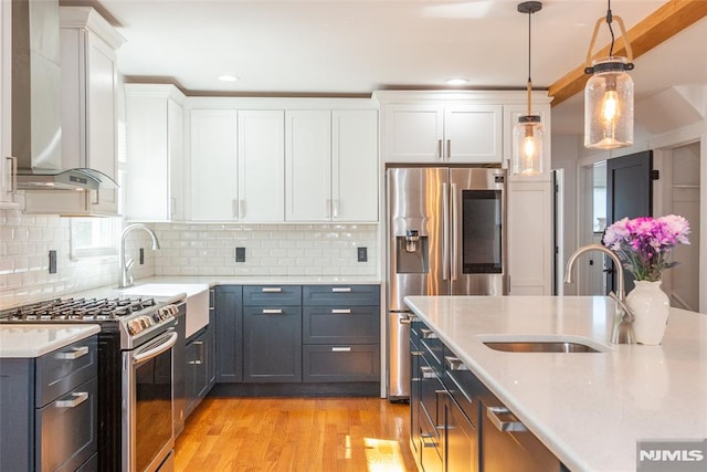 kitchen featuring light wood finished floors, white cabinets, stainless steel appliances, pendant lighting, and a sink