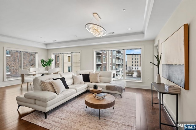 living area with a notable chandelier, dark wood-style flooring, visible vents, baseboards, and a tray ceiling