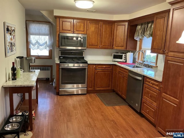 kitchen featuring brown cabinets, radiator heating unit, appliances with stainless steel finishes, a sink, and wood finished floors