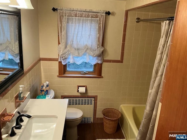 bathroom with toilet, tile walls, vanity, radiator, and shower / bathtub combination with curtain