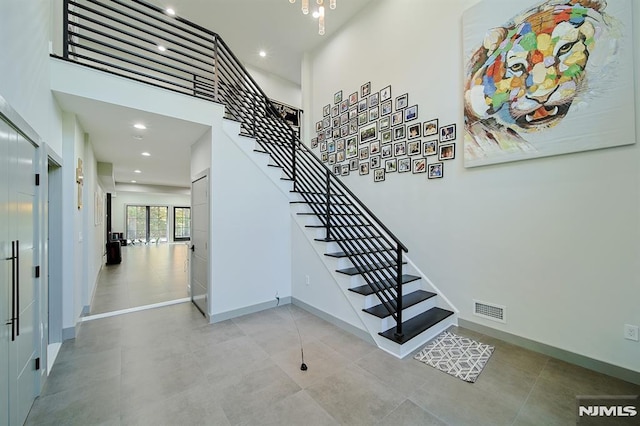 stairway with recessed lighting, visible vents, baseboards, and a towering ceiling