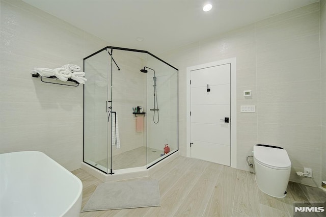 bathroom with toilet, wood finished floors, tile walls, a shower stall, and a soaking tub