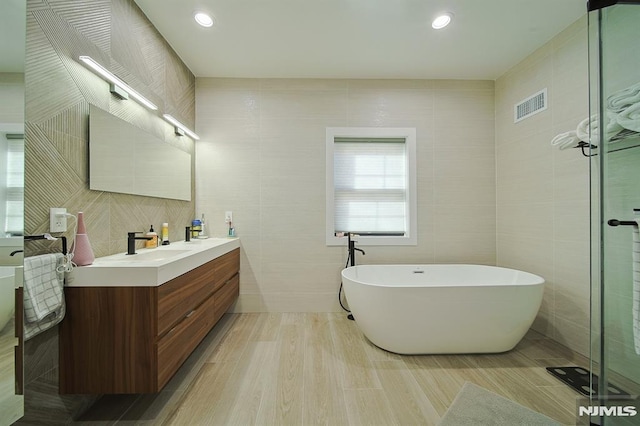 bathroom featuring vanity, tile walls, visible vents, and a freestanding bath