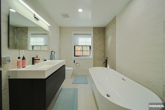 full bath featuring vanity, visible vents, a soaking tub, tile walls, and toilet