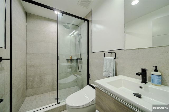 bathroom featuring visible vents, toilet, vanity, a stall shower, and tile walls