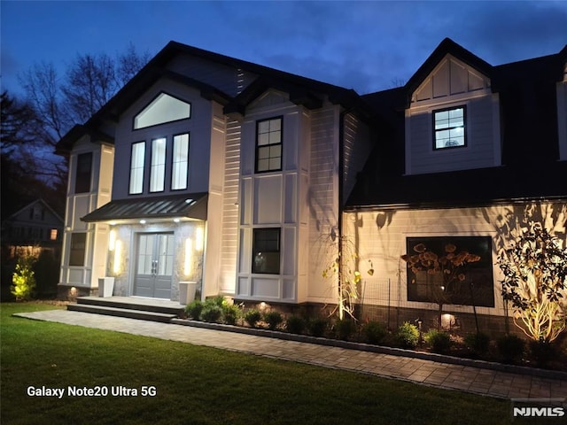 view of front of house with board and batten siding, a front lawn, french doors, metal roof, and a standing seam roof