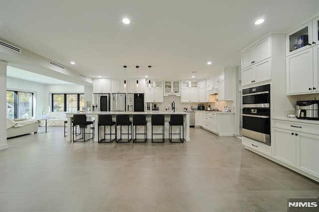 kitchen with visible vents, an island with sink, a kitchen bar, appliances with stainless steel finishes, and white cabinets