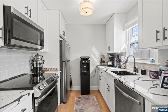 kitchen featuring stainless steel appliances, light stone counters, a sink, and white cabinets