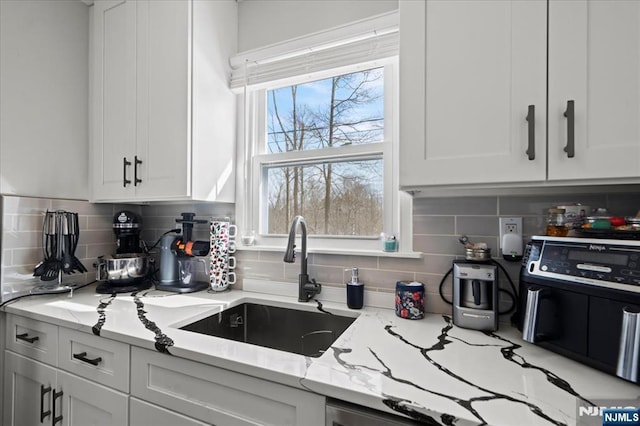 kitchen with light stone counters, decorative backsplash, a sink, and white cabinets