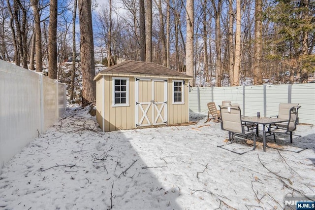 snow covered structure featuring an outbuilding, a fenced backyard, and a shed