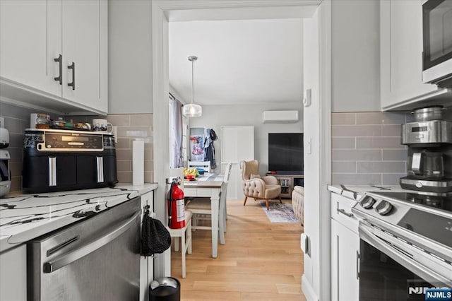 kitchen featuring a wall unit AC, stainless steel appliances, white cabinetry, light stone countertops, and light wood-type flooring