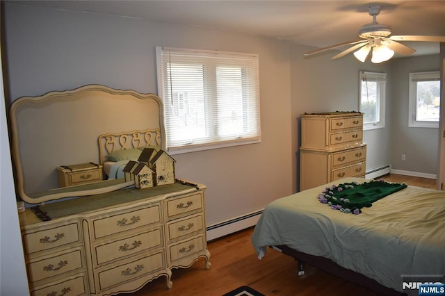 bedroom featuring a baseboard heating unit, multiple windows, and light wood-style flooring