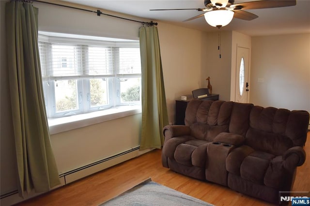 living area with ceiling fan, a baseboard heating unit, and wood finished floors