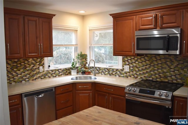 kitchen featuring butcher block countertops, a sink, appliances with stainless steel finishes, brown cabinets, and tasteful backsplash