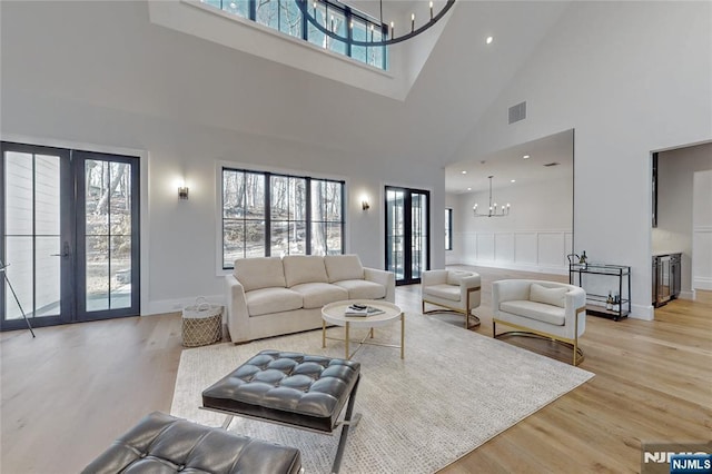 living area featuring a notable chandelier, wood finished floors, visible vents, and french doors