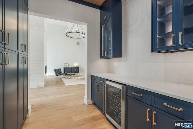 kitchen with beverage cooler, blue cabinetry, light countertops, light wood-style floors, and a chandelier