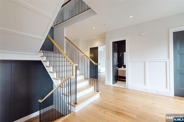 staircase with wainscoting, a decorative wall, recessed lighting, and wood finished floors