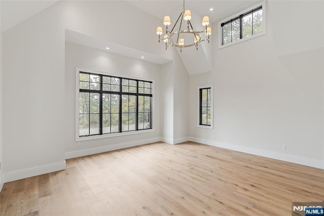 unfurnished room featuring baseboards, recessed lighting, light wood-style floors, a towering ceiling, and a chandelier