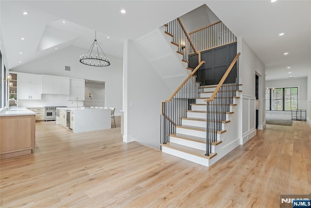 stairs with visible vents, a chandelier, recessed lighting, wood finished floors, and high vaulted ceiling