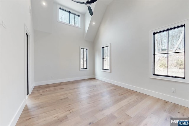 empty room featuring baseboards, a high ceiling, ceiling fan, and light wood finished floors