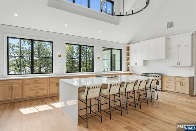 kitchen with stainless steel range, a breakfast bar area, a kitchen island with sink, and light wood finished floors