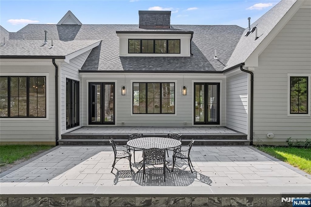 rear view of house with a deck, a patio area, french doors, and roof with shingles