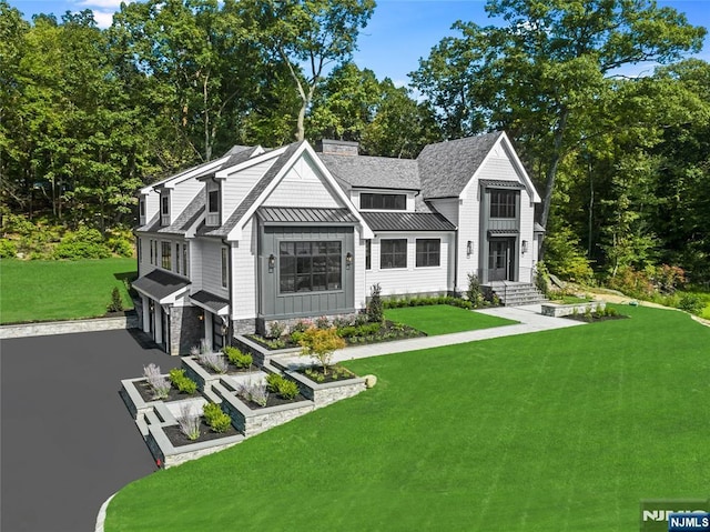 exterior space featuring aphalt driveway, a front yard, metal roof, a garage, and a standing seam roof